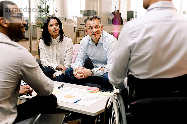 Geschäftskollegen betrachten einen behinderten Vertriebsleiter während einer Besprechung im Büro