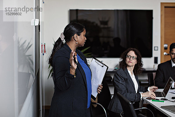 Geschäftsfrau hält Klemmbrett in der Hand  während sie bei einer Besprechung im Büro mit Kollegen diskutiert