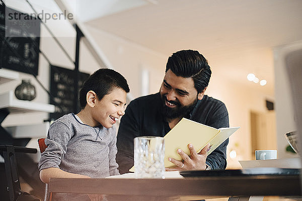 Lächelnder Vater unterrichtet autistischen Sohn  während er im Haus am Tisch sitzt
