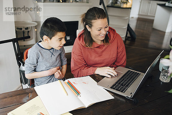 Lächelnde Mutter zeigt ihrem autistischen Sohn ein Video auf einem Laptop zu Hause