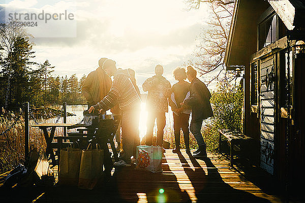 Scherenschnitt-Freunde unterhalten sich  während sie bei Sonnenuntergang vor der Hütte vor dem See stehen