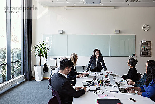 Geschäftsfrau interagiert mit Kollegen  die während einer Sitzung im Sitzungssaal am Konferenztisch sitzen