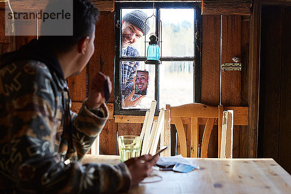 Mann zeigt einem Freund  der in einer Hütte sitzt  ein Foto über ein Smartphone