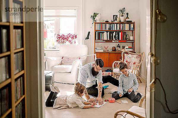 Vater zeichnet mit Töchtern  während er sich zu Hause im Wohnzimmer ausruht