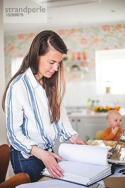 Vielbeschäftigte Unternehmerin prüft eingereichte Dokumente  während die Tochter im Hintergrund im Home-Office sitzt