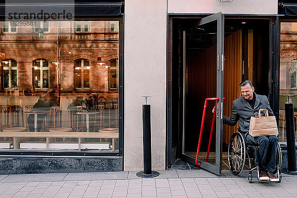 Behinderter reifer Mann mit Einkaufstasche verlässt Laden in der Stadt