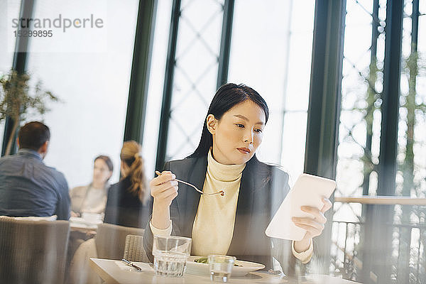 Zuversichtliche Geschäftsfrau benutzt digitales Tablet beim Mittagessen in der Cafeteria im Büro
