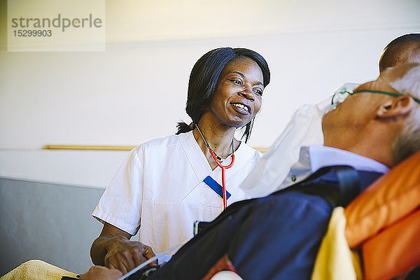 Lächelnde Ärztin betrachtet reife Patientin auf Bahre im Krankenhaus