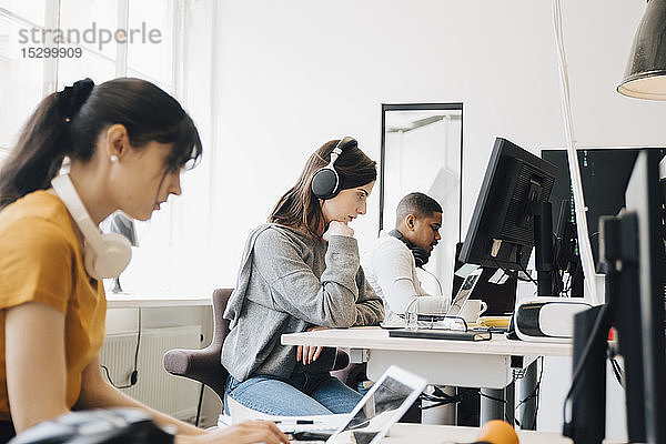 Seitenansicht von fokussierten Programmierern  die Laptops am Schreibtisch benutzen  während sie im Büro sitzen