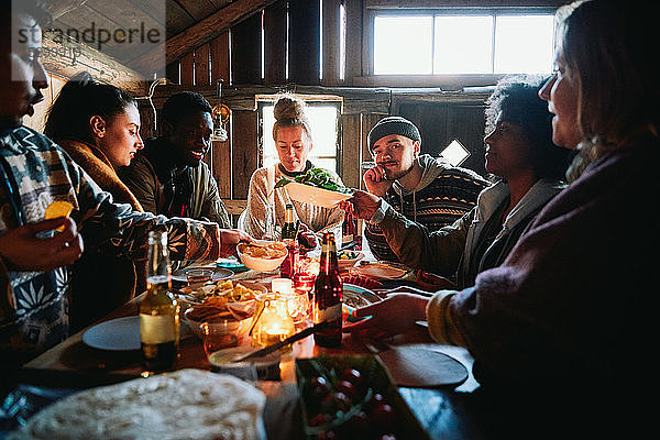Männliche und weibliche Freunde unterhalten sich beim Essen in der Hütte am Wochenende