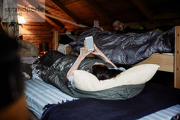 Freundinnen und Freunde benutzen Smartphones  während sie in einer Hütte liegen