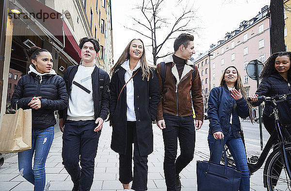Lächelnde männliche und weibliche Teenager-Freunde gehen auf einem Fußweg in der Stadt
