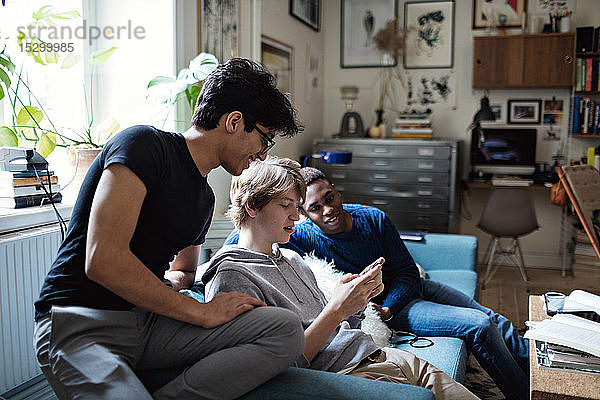 Freunde sehen einen Teenager an  der soziale Medien nutzt  während er zu Hause im Wohnzimmer lernt