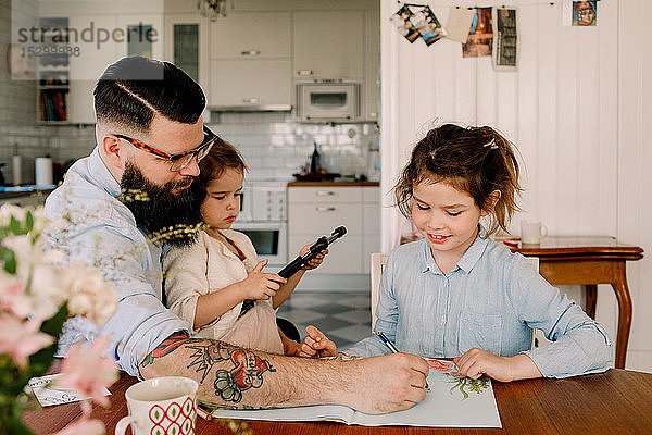 Vater hilft Mädchen bei den Hausaufgaben  während er mit Tochter am Esstisch sitzt