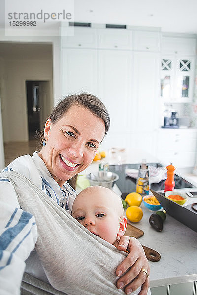 Porträt einer lächelnden Food-Bloggerin  die ihre Tochter zu Hause in der Küche trägt