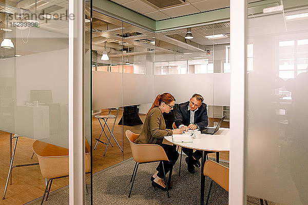 Vertriebsleiter diskutieren über Geschäftspläne  während sie am Arbeitsplatz mit Blick durch die Tür sitzen