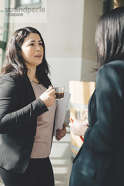 Berufstätige Frauen beim Kaffee trinken  während sie im Bürokorridor diskutieren