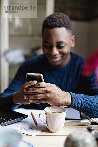 Lächelnder Teenager nutzt soziale Medien auf Smartphones beim Lernen zu Hause