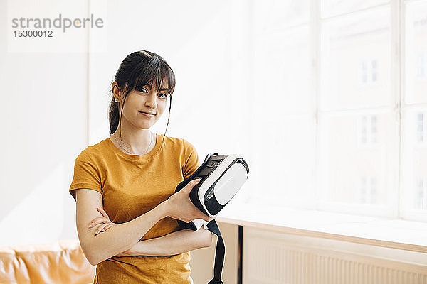 Porträt einer Unternehmerin  die einen Virtual-Reality-Simulator hält  während sie am Fenster steht