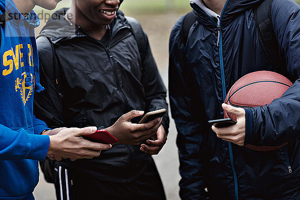 Ein Teil der Freunde hält Smartphones in der Hand  während sie auf dem Basketballplatz stehen