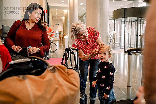 Lächelnde Mutter sieht ältere Frau an  die im Hotel steht und der Tochter die Haare bindet