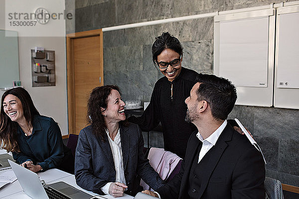 Lächelnde Geschäftsfrau interagiert mit fröhlichen Kollegen im Büro