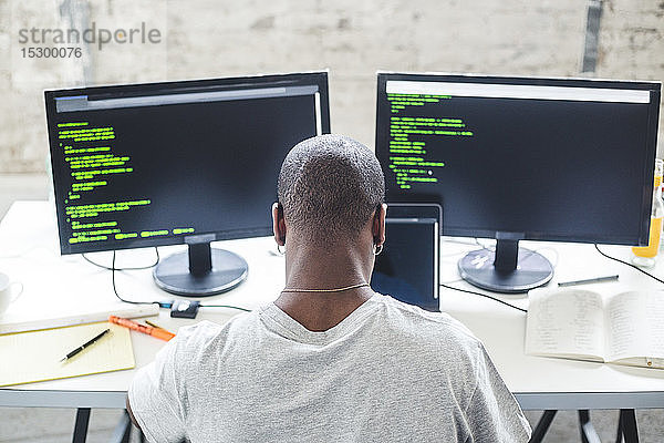 Hochwinkelansicht eines Computerprogrammierers mit rasiertem Kopf  der Codes am Schreibtisch im Büro programmiert