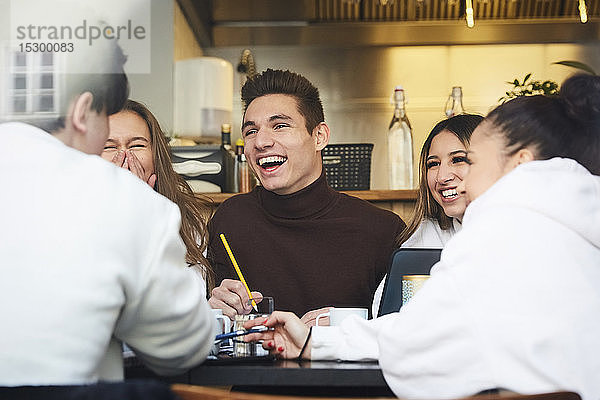Männliche und weibliche Freunde im Teenageralter lächeln beim Lernen am Tisch im Café