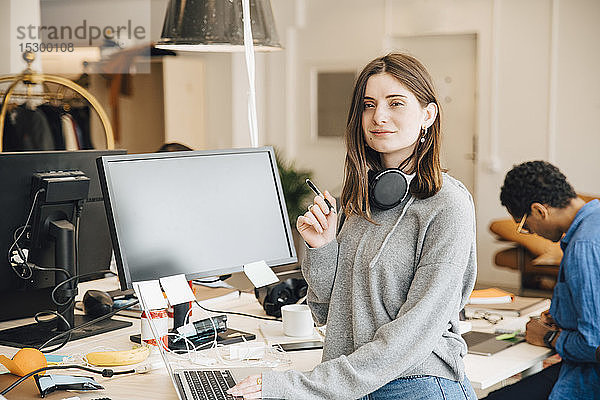 Porträt einer lächelnden Computerprogrammiererin mit Laptop am Schreibtisch im Büro