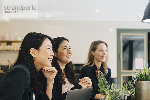 Lächelnde Geschäftsfrauen sitzen in einer Sitzung am Konferenztisch