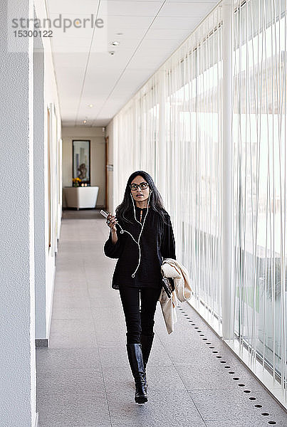 Geschäftsfrau in voller Länge  die im Büro auf dem Flur mit einem Smartphone spricht