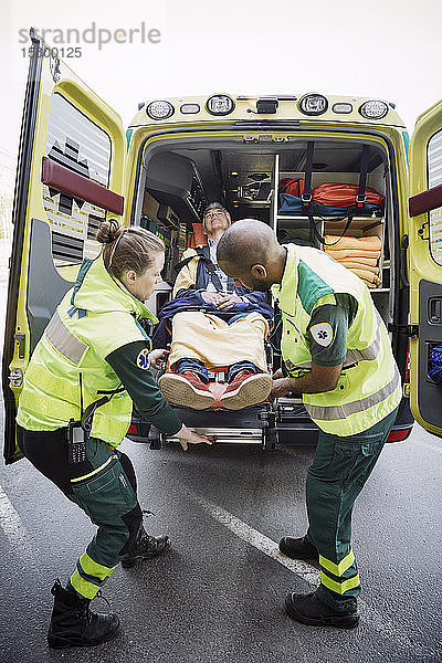 Männliche und weibliche Rettungssanitäter in voller Länge beim Entladen des Patienten aus dem Krankenwagen