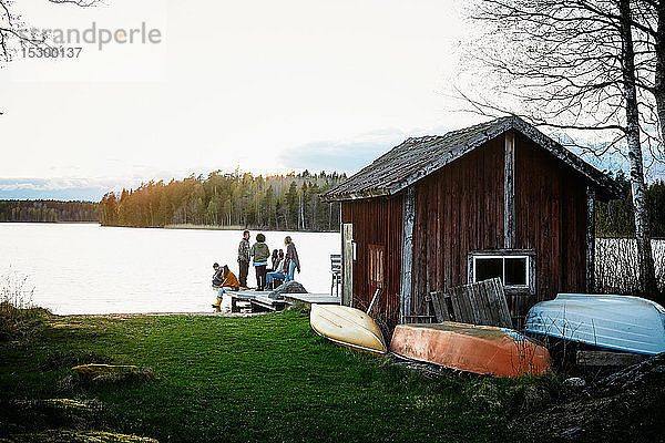 Freunde und Freundinnen unterhalten sich bei Sonnenuntergang vor der Hütte am See