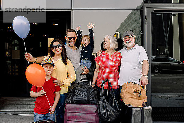 Porträt einer fröhlichen Familie mit Gepäck  die während des Urlaubs am Hoteleingang steht