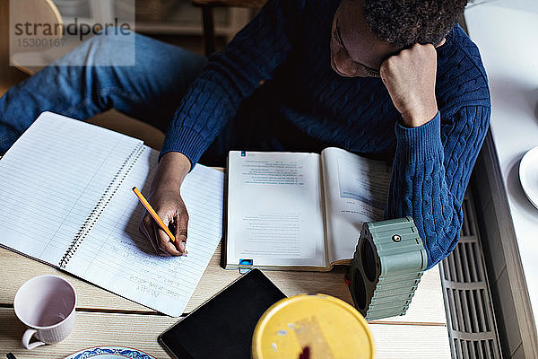 Schrägansicht eines Teenagers  der während der Hausaufgaben auf ein Buch schreibt