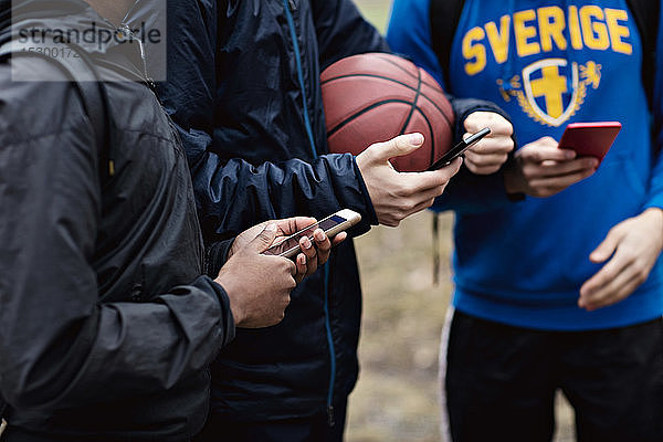 Mitten unter telefonabhängigen Freunden  die warme Kleidung tragen  während sie auf dem Basketballplatz stehen