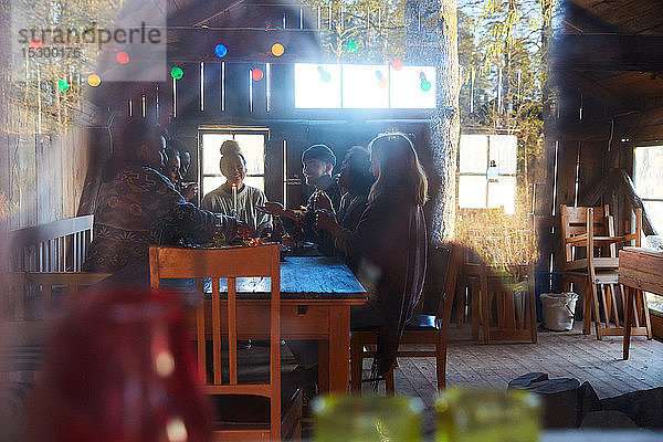 Männliche und weibliche Freunde unterhalten sich bei Tisch in einer durchs Fenster gesehenen Hütte