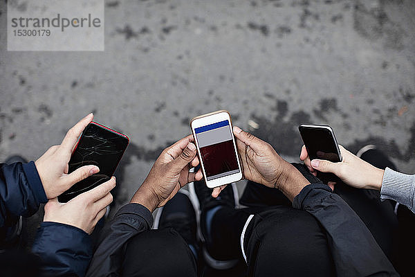 Schrägansicht von Freunden  die soziale Medien in Mobiltelefonen auf der Straße nutzen