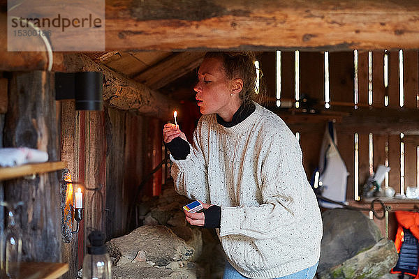 Mittelgroße erwachsene Frau  die im Ferienhaus stehend Streichhölzer bläst