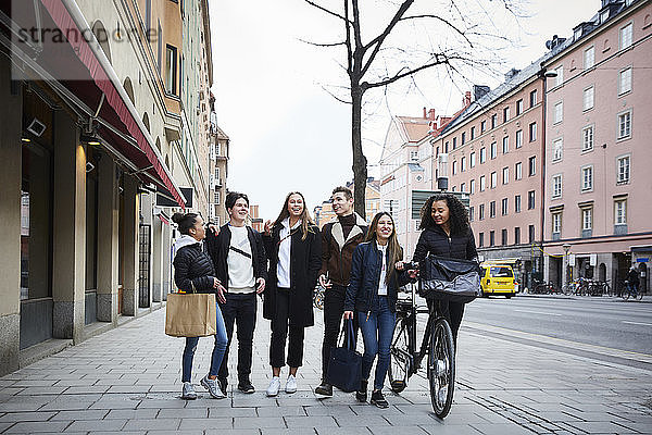 Lächelnde männliche und weibliche Teenager-Freunde gehen in der Stadt auf dem Bürgersteig