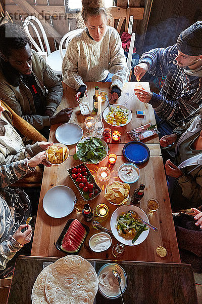 Schrägaufnahme von Freunden bei Essen und Trinken  während sie in einer Hütte sitzen