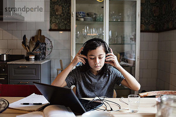 Junge benutzt Kopfhörer bei den Hausaufgaben zu Hause