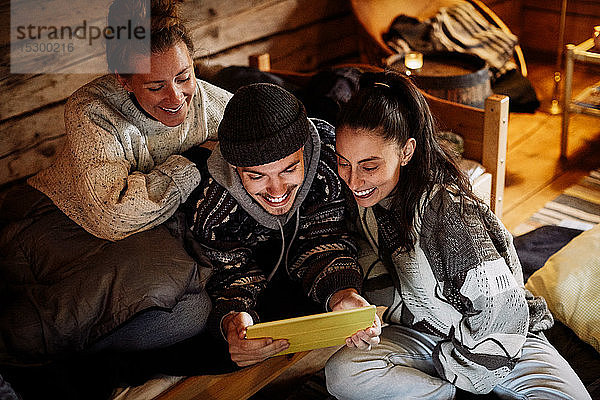 Hochwinkelansicht von lächelnden Freunden  die über ein digitales Tablet einen Film ansehen  während sie sich in einem Ferienhaus entspannen
