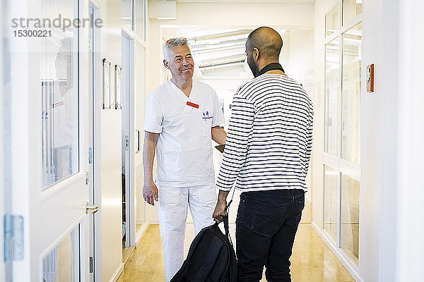 Lächelndes medizinisches Personal schaut den männlichen Patienten während eines Besuchs im Krankenhauskorridor an