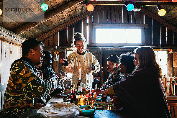 Lächelnde junge Frau unterhält sich beim Essen mit Freunden in einer Hütte