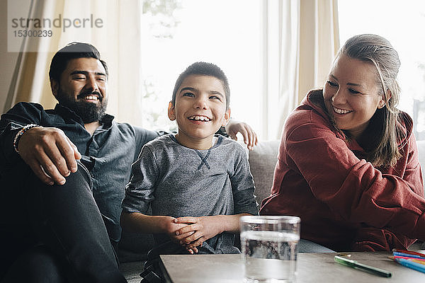 Lächelnde Eltern sehen ihren autistischen Sohn an  während sie auf dem Sofa im Wohnzimmer sitzen