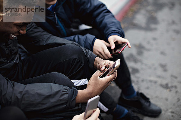 Social-Media-süchtige männliche Freunde sitzen im Winter in der Stadt auf der Straße