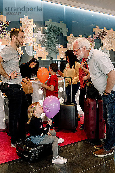 Großvater im Gespräch mit einem Mädchen  das einen Ballon hält  während es im Hotel auf einem Koffer sitzt