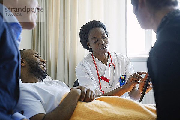 Ärztin erklärt Patientin und Familie auf der Krankenhausstation die Krankenakte über ein digitales Tablett