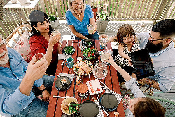 Hochwinkelansicht einer Familie  die auf Trinkgläser anstößt  während sie auf der Terrasse am Tisch sitzt